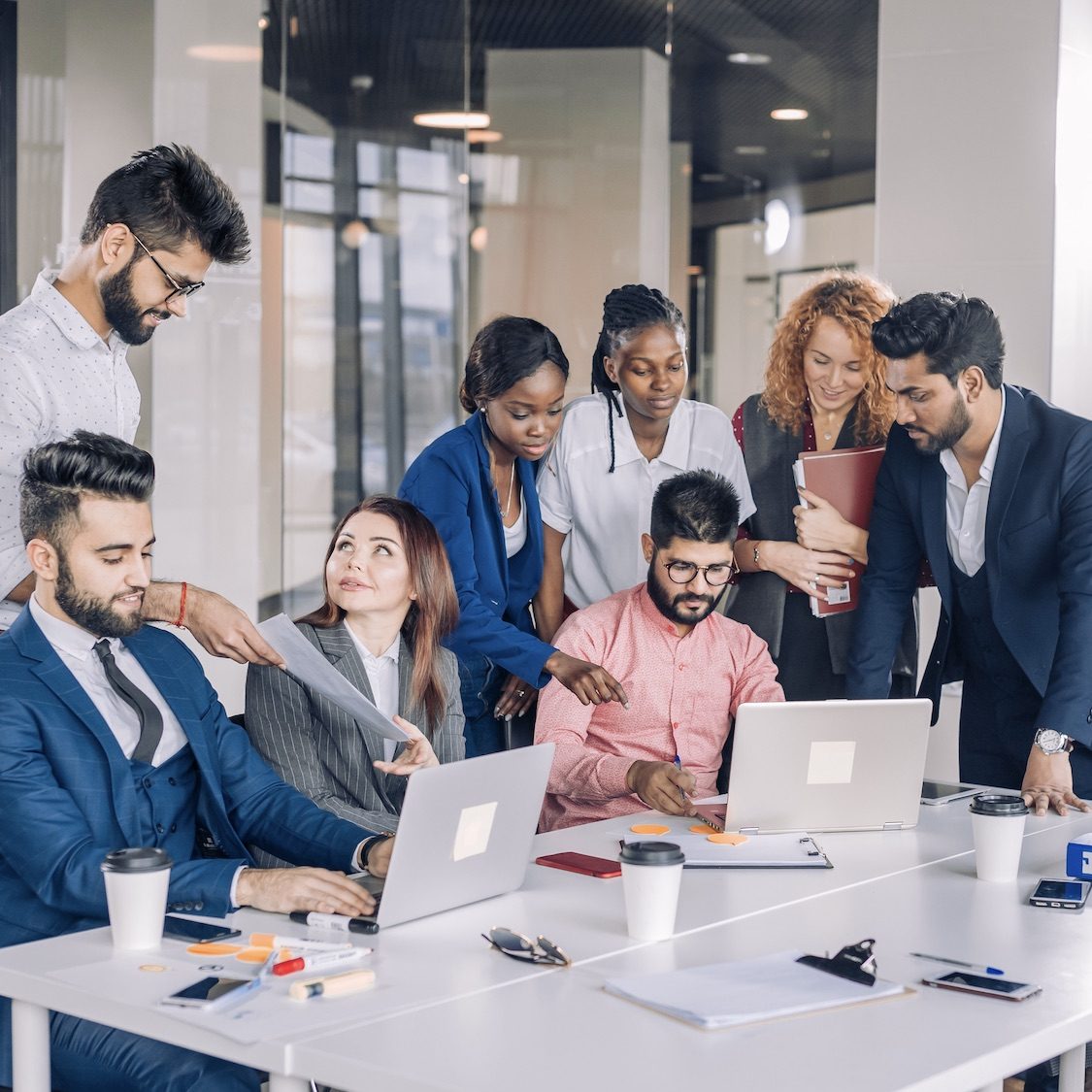 Young multi-ethnic work team exchanges ideas gathering around laptop computers