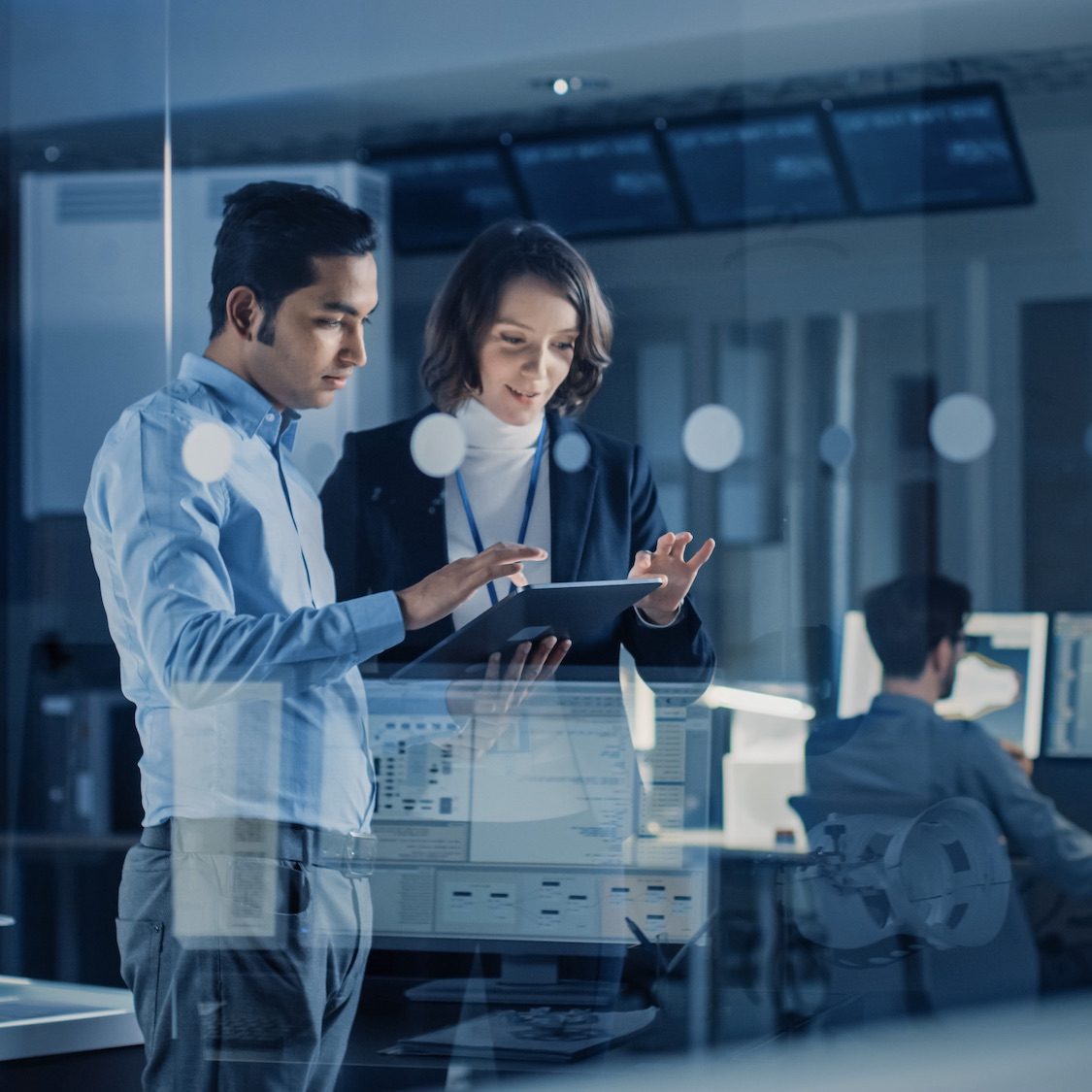 In Technology Research Facility: Female Project Manager Talks With Chief Engineer, they Consult Tablet Computer. Team of Industrial Engineers, Developers Work on Engine Design Using Computers